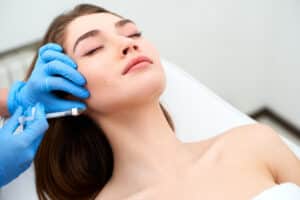 Woman laying down with eyes closed as specialist administers RHA filler injections in the face